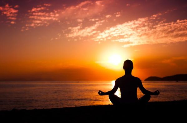 Person meditating in front of an orange sunset